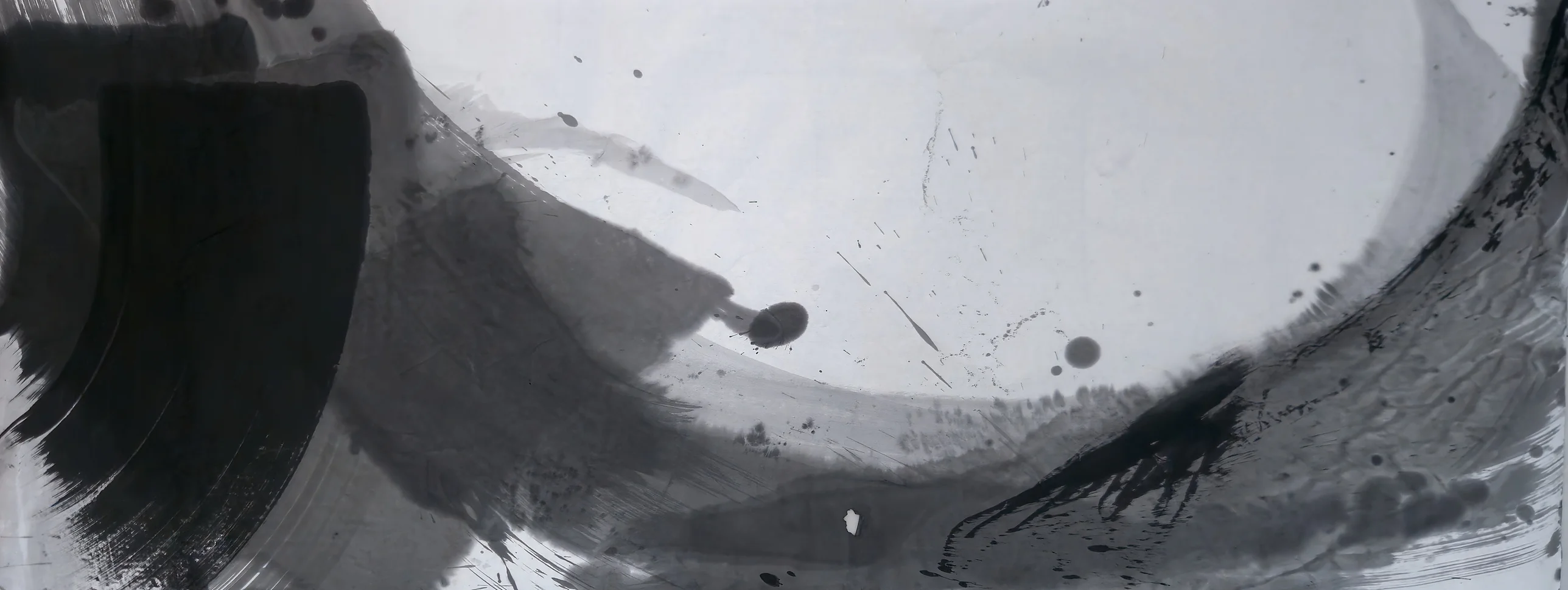 Wide ink painting: black block at left, grey sweep along the bottom curving up the right edge around pale empty paper, with scattered drops.