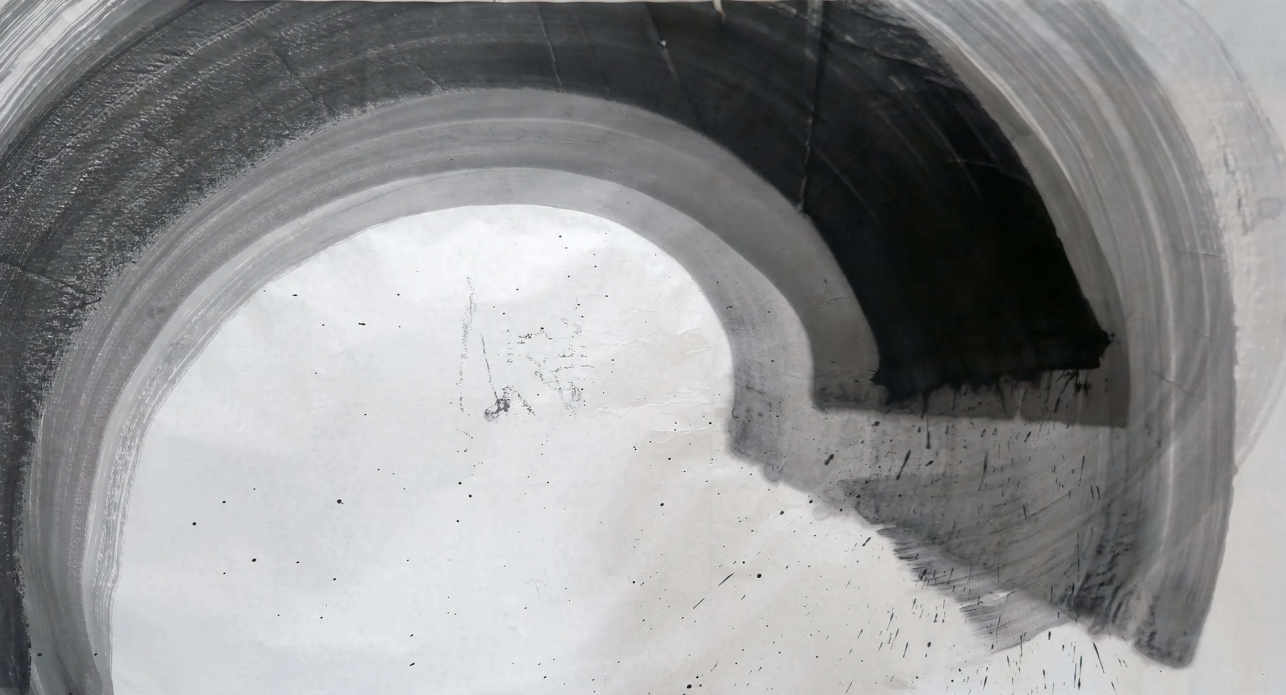 A wide grey arc sweeps from lower left over the top into a squared black mass at upper right, enclosing pale paper, with spatter lower right.
