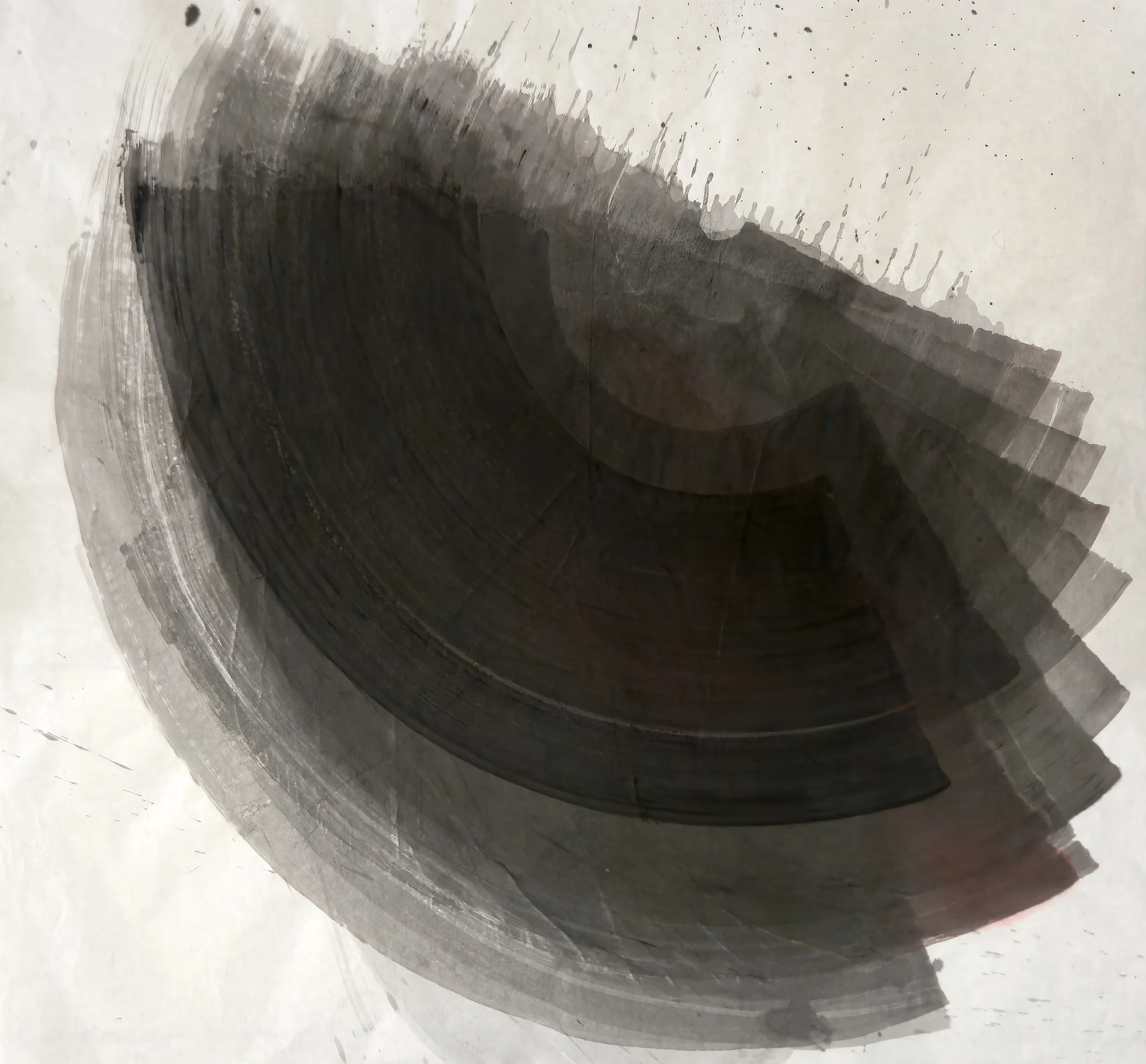 A large dark grey fan of curved brushstrokes sweeps from upper left to right across pale paper, with drips and spatter toward the upper right.